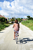 Junge Frau fährt Fahrrad auf der Insel Taketomi, Präfektur Okinawa, Japan