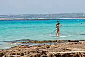 Junge Frau beim Paddelsurfen am Strand von Migjorn, Formentera
