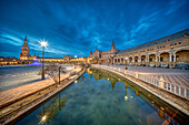 Atemberaubende Dämmerungsszene auf der historischen Plaza de EspaUa mit spiegelnden Wasserflächen, Sevilla, Spanien