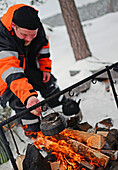 Antti, young guide from VisitInari, prepare coffee and tea on a fire in the wilderness of Lake Inari, Lapland, Finland
