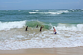 Drei Einheimische und ein Tourist spielen mit den Wellen am Strand von Unawatuna, Sri Lanka
