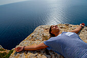 Junge Frau entspannt sich auf einem Felsen an der Küste, Formentera