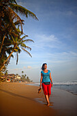 Junge Frau beim Spaziergang am Strand von Hikkaduwa bei Sonnenuntergang, Sri Lanka