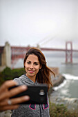 Young woman takes a selfie with Golden Gate Bridge, San Francisco.
