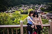 Zwei Mädchen machen ein Selfie von einem Aussichtspunkt in Shirakawa-go, einem traditionellen Dorf, das einen als Gassho-Zukuri bekannten Baustil zeigt, Präfektur Gifu, Japan