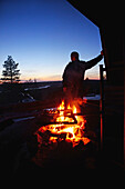 J?nk?l? entspannt sich bei einem Halt am Feuer. Schneemobil-Sonnenuntergangstour mit Arctic Lifestyle, Rovaniemi, Lappland, Finnland