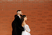 Seitenansicht von Braut und Bräutigam vor einer Backsteinmauer