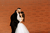 Bride and groom embracing against brick wall