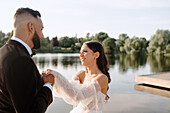 Braut und Bräutigam halten sich am Seeufer an den Händen