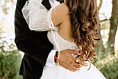 Mid section of bride and groom embracing in park