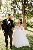 Smiling bride and groom walking in park