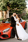 Brie and groom kissing at red car