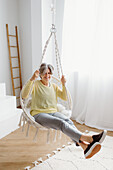 Portrait of smiling woman sitting in swing chair at home