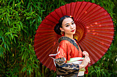 Porträt einer lächelnden Frau mit Kimono und Sonnenschirm in der Hand