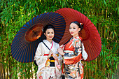 Portrait of two women wearing kimonos and holding parasols in park