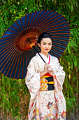Porträt einer lächelnden Frau in Kimono und mit Sonnenschirm im Park