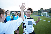 UK, Female soccer team members (10-11, 12-13) giving high five in field