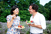 Lächelndes reifes Paar isst Früchte in einem Lavendelfeld