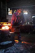 Ein Arbeiter formt einen Stahlknüppel auf einem 5 Tonnen schweren Freiflächenhammer vor, bevor er einem Satz von zwei Gesenken zum Schmieden im Hammer zugeführt wird