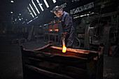 Forge worker preparing to release finished upset forging into steel container