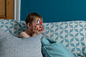Porträt eines Jungen (18-23 Monate) mit bemaltem Gesicht, der auf dem Sofa sitzt