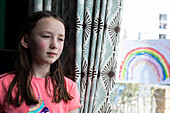 Girl (4-5) by window with drawing of rainbow