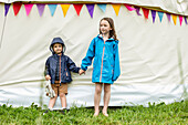 Sister (4-5) and brother (18-23 months) holding hands outside tent