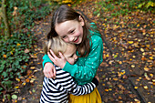 Sister (4-5) and brother (18-23 months) hugging outdoors