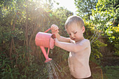 Hemdloser Junge (18-23 Monate) gießt Wasser aus einer Gießkanne im Garten