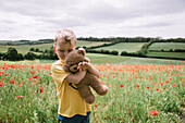 Boy (18-23 months) hugging teddy bear in poppy field