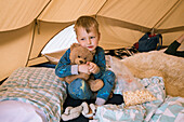 Junge (18-23 Monate) umarmt Teddybär im Zelt