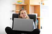 Lächelnde junge Frau, die zu Hause einen Laptop benutzt