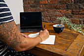 Close-up of woman typing on laptop and holding coffee cup