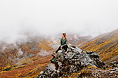 Kanada, Yukon, Whitehorse, Frau sitzt auf einem Felsen in nebliger Landschaft