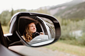 Canada, Yukon, Whitehorse, Smiling woman with camera reflected in car mirror