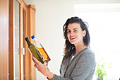 Smiling woman holding two bottles of live oil at home