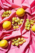 Draufsicht auf Zitronen und Weintrauben auf rosa Tischtuch