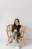 Studioaufnahme einer jungen Frau, die in einem Korbstuhl sitzt