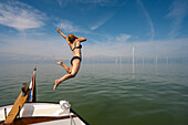 Niederlande, Friesland, Breezanddijk, Mädchen springt in der Nähe von Windkraftanlagen ins Meer