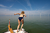 Niederlande, Friesland, Breezanddijk, Mädchen springt von Boot in der Nähe von Windkraftanlagen