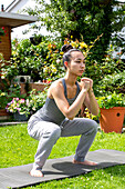 UK, London, Woman doing squats on lawn in front of house