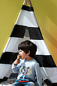 UK, Boy (4-5) eating ice cream in front of striped teepee