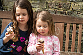 UK, Zwei Mädchen (2-3, 4-5) mit Eiswaffeln auf einer Bank
