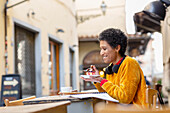 Italien, Toskana, Pistoia, Frau sitzt in einem Straßencafé und isst ein Dessert