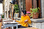 Italien, Toskana, Pistoia, Frau mit Kopfhörern in einem Straßencafé