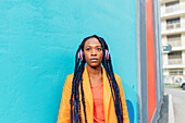 Italy, Milan, Portrait of stylish woman with headphones in front of blue wall