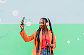 Italy, Milan, Stylish woman with headphones holding smart phone in front of wall