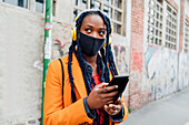 Italy, Milan, Woman with headphones and face mask holding smart phone