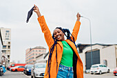 Italy, Milan, Fashionable woman holding face mask and smiling on street