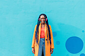 Italy, Milan, Portrait of stylish woman with headphones in front of blue wall